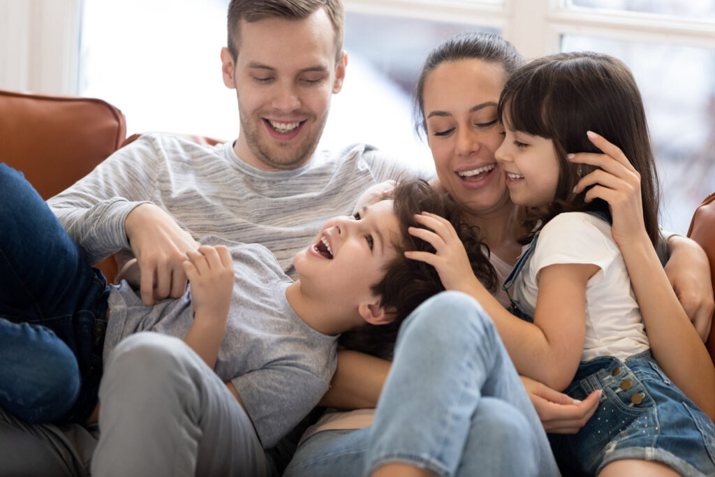 happy mum dad having fun with kids tickling on sofa