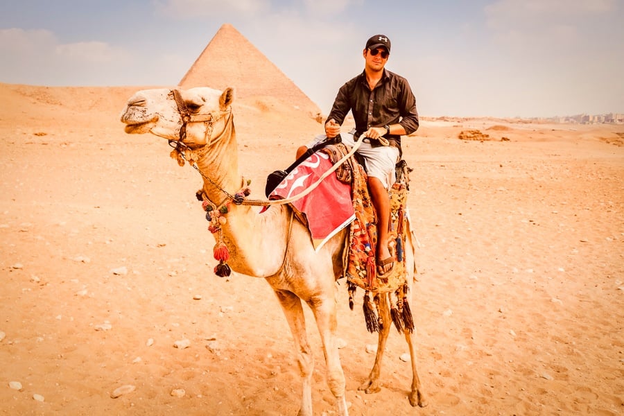 Travel guy riding a camel at the Great Pyramids of Giza in Egypt